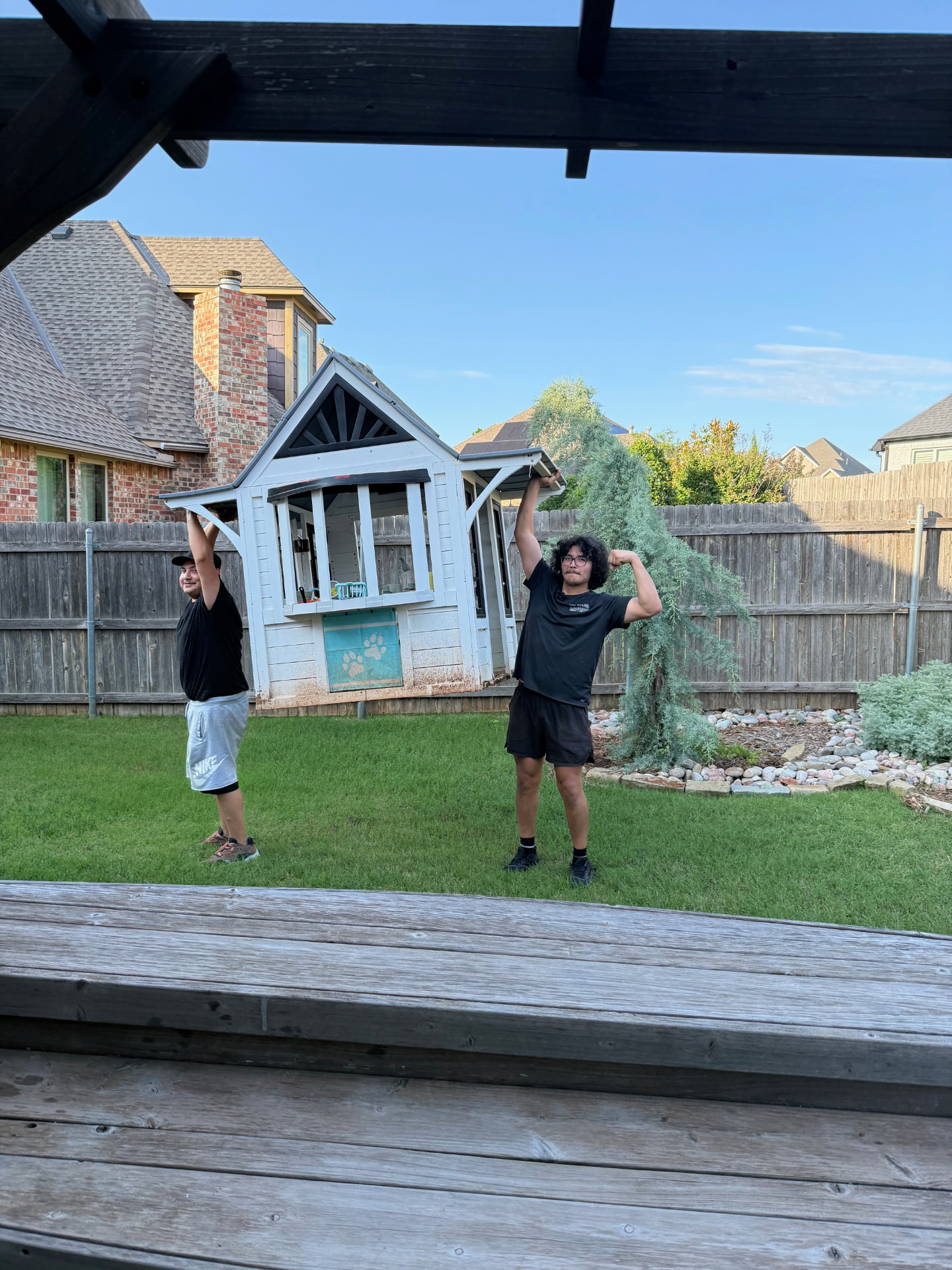 Two Top Dawg movers carrying a backyard playhouse in an Oklahoma City neighborhood